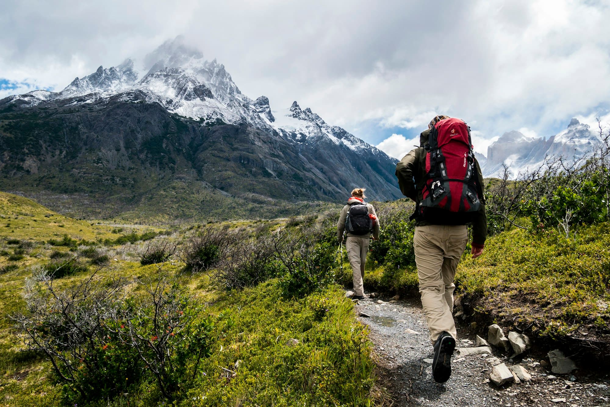 Hikers walking a green mountain trail toward misty forested hills