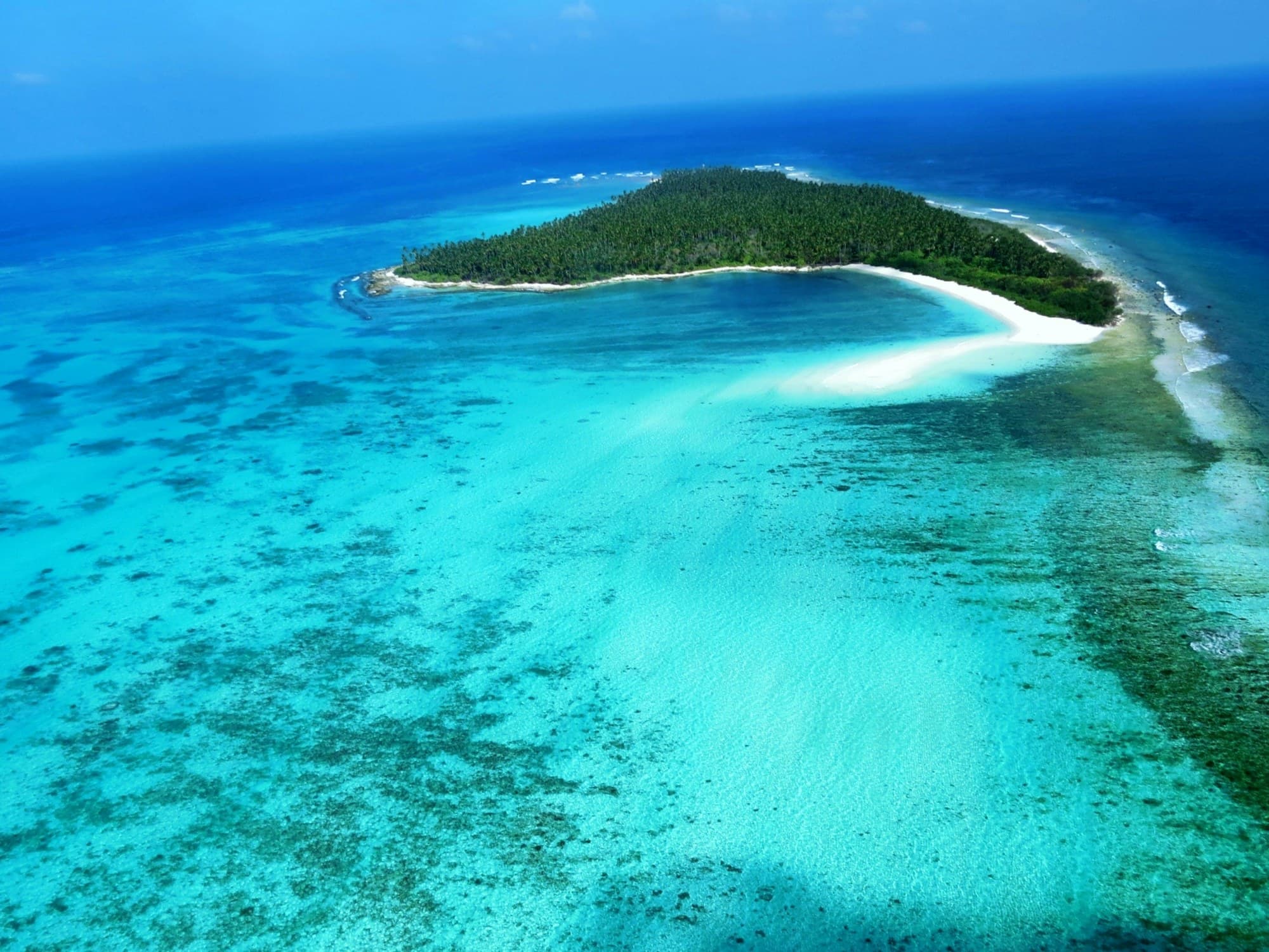 Aerial view of a turquoise reef and white-sand island in the Indian Ocean