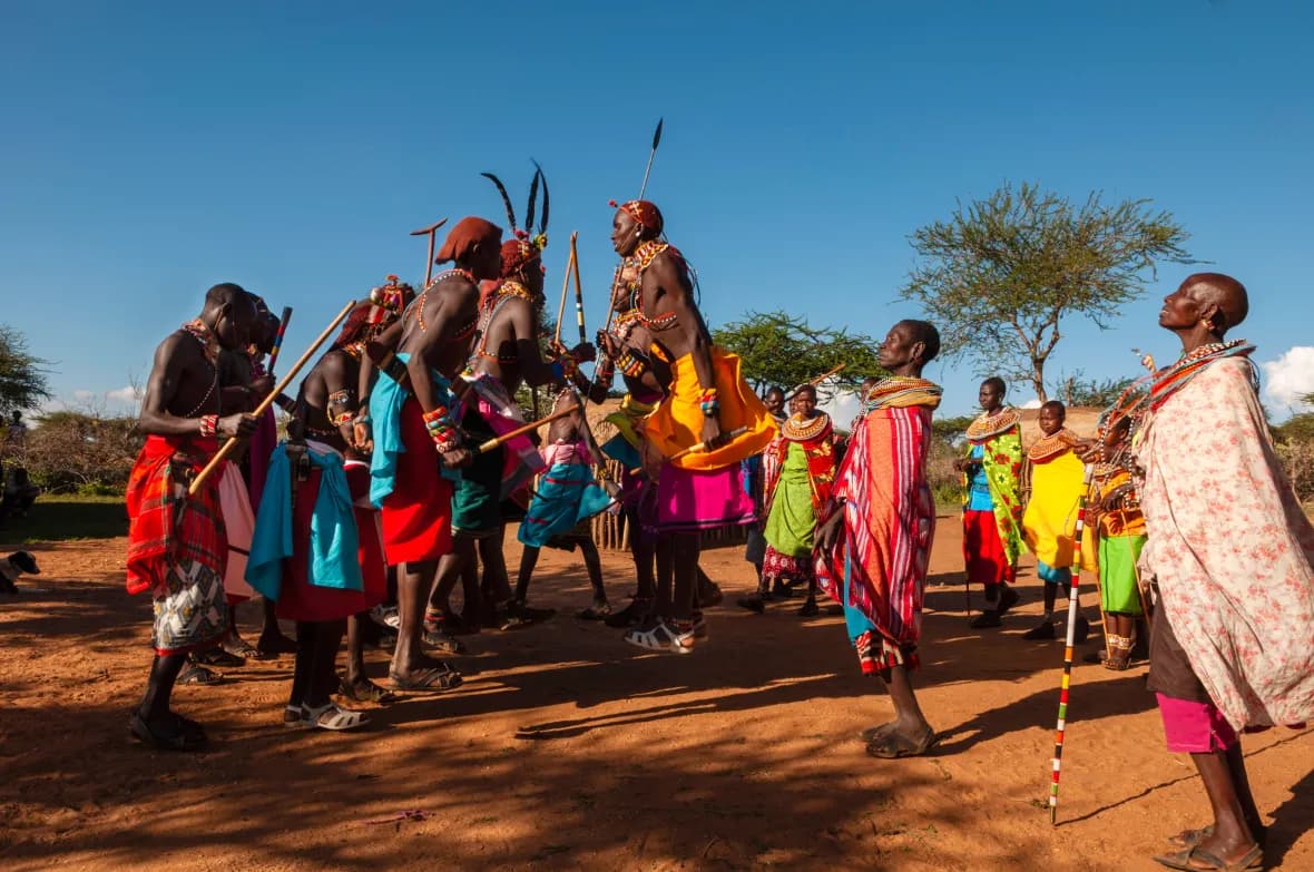 Men and women in traditional beaded dress dancing together during a community cultural visit
